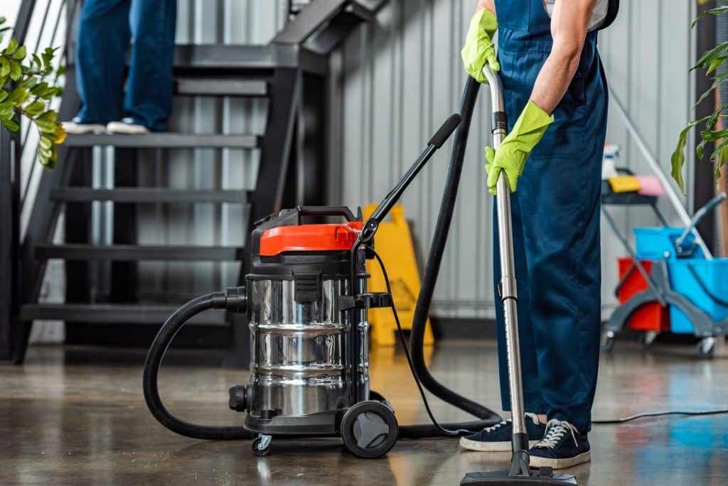 cropped view of cleaner in uniform cleaning floor with vacuum cleaner
